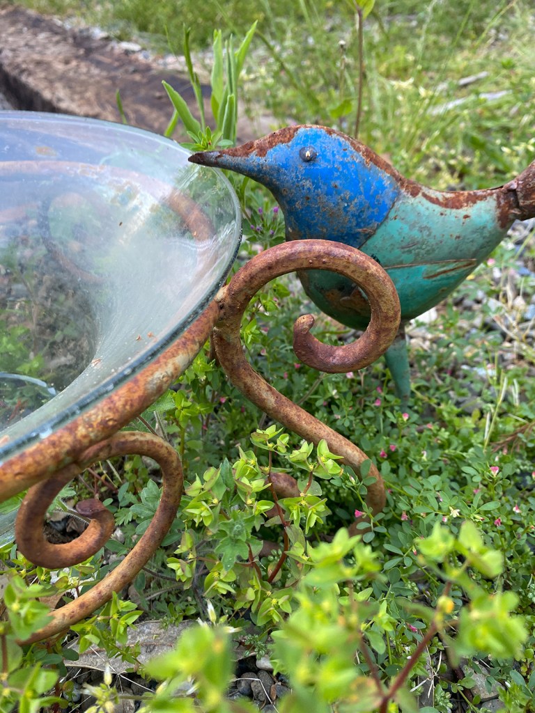metal blue and green bird drinking water from a glass fountain