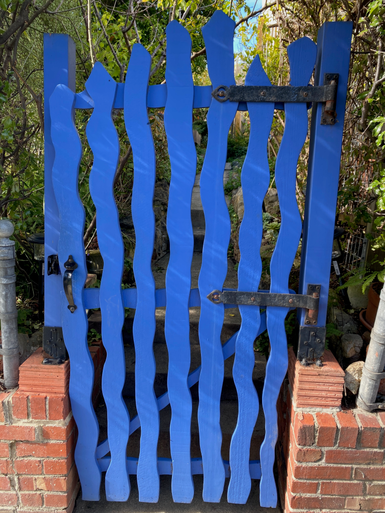 blue squiggly wood gate with brick wall and green trees